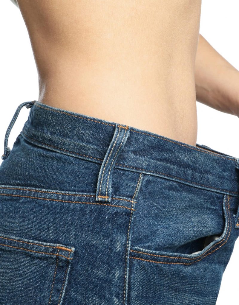 Girl pulling her big jeans and showing weight loss, isolated on white background
